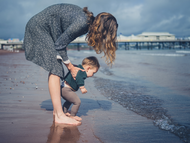 Une mère aide son bébé à marcher sur la plage
