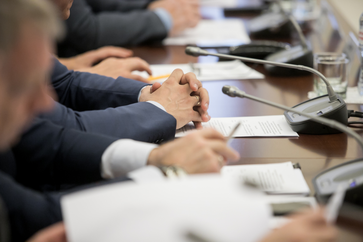 Loi Climat– Hommes en costume qui croisent les mains sur une bureau avec micro