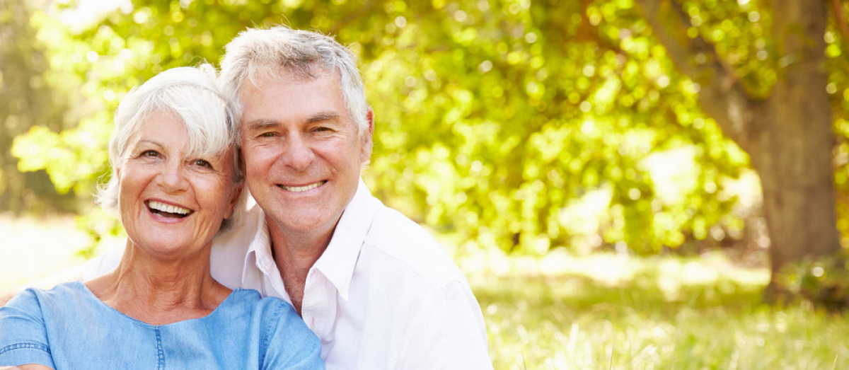 Prêt immobilier après 60 ans – Un couple de séniors assis dans l’herbe en train de sourire