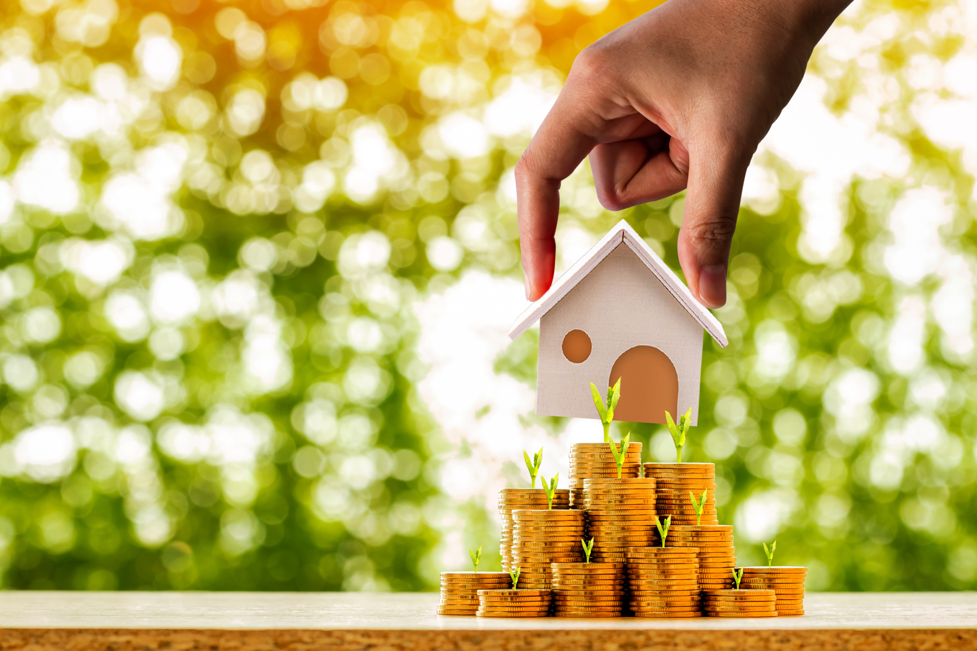 Une personne pose une figurine de maison sur un tas de pièces de monnaie