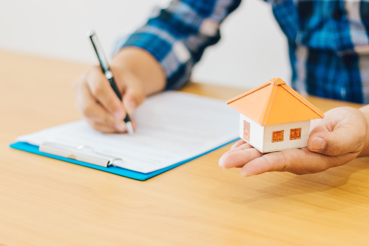 Comment choisir son locataire – Une personne écrit en portant une maison miniature