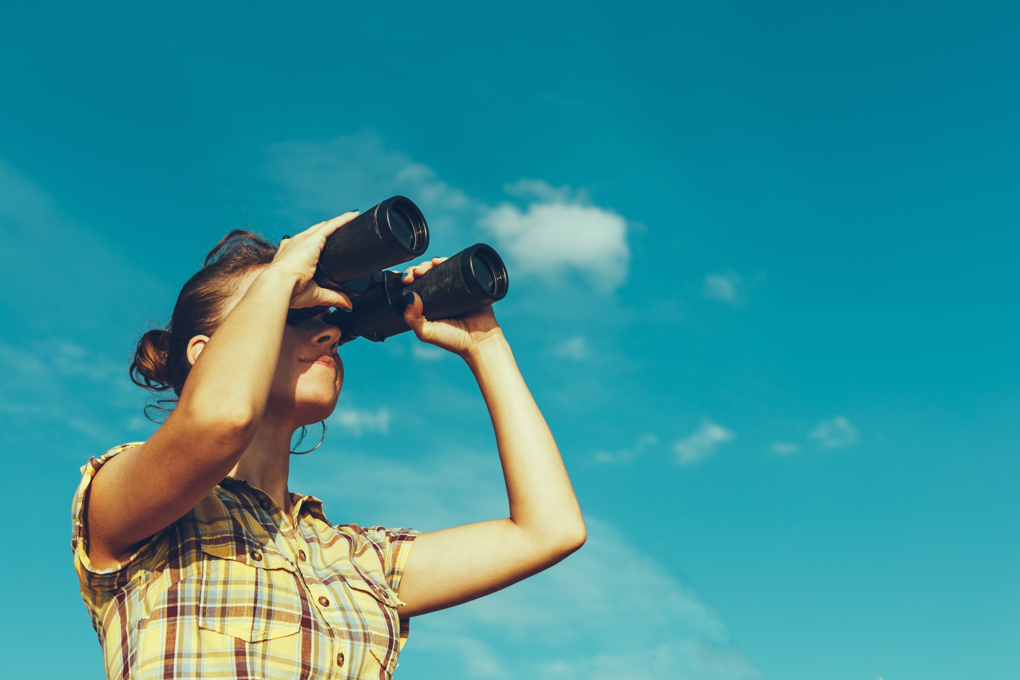 femme regardant l’avenir sur fond de ciel bleu avec des jumelles