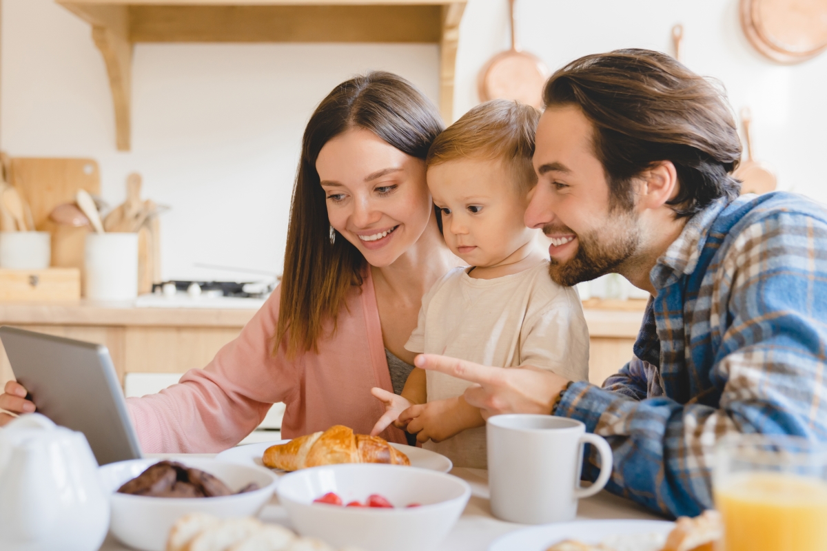 une famille consulte le site d’un commercialisateur en immobilier neuf à la table du petit déjeuner