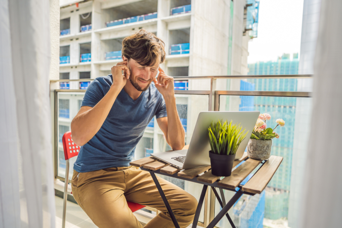 norme acoustique logement neuf – un homme sur son balcon qui se bouche les oreilles