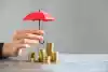 Une personne tenant un parapluie miniature protège un tas de pièces de monnaie