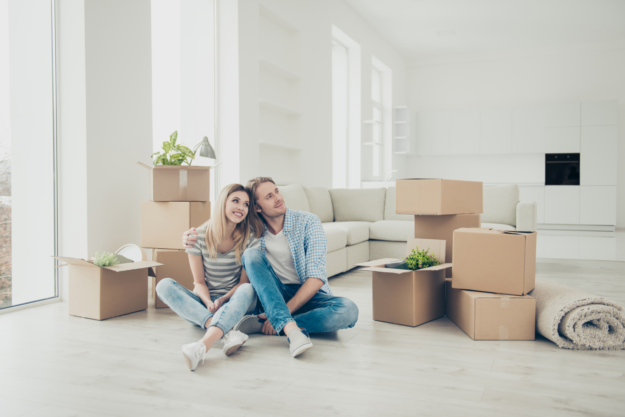 un couple emménage dans son appartement neuf. Ils sont assis sur le sol devant un canapé avec des cartons.