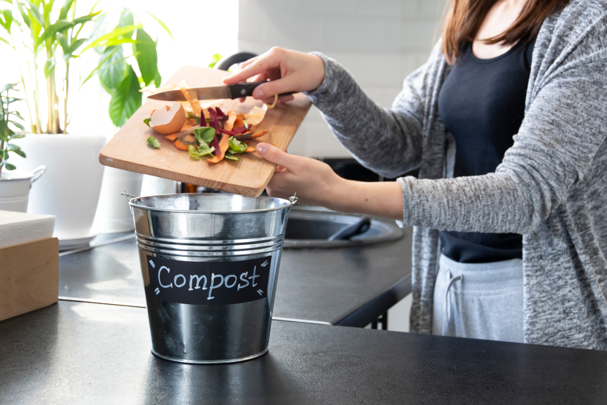 une femme jette des pelures de légumes dans un seau à compost au sein de sa cuisine