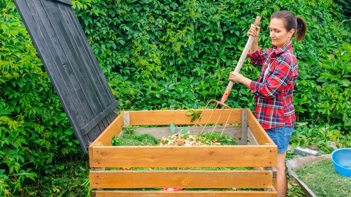 une femme remue du compost dans un bac de bois