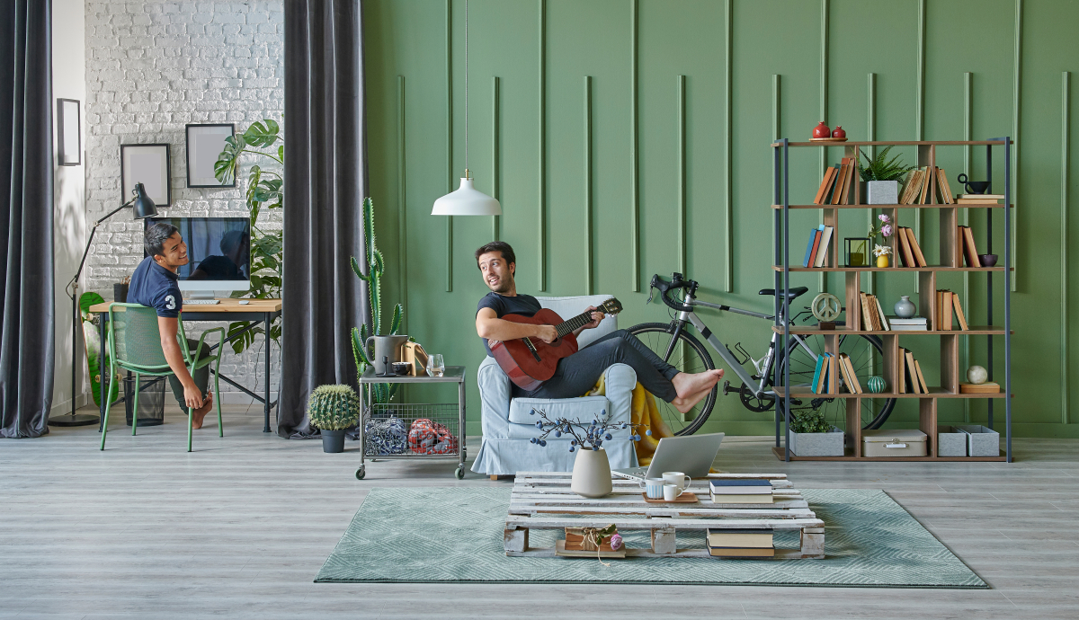 un étudiant dans un salon commun qui joue de la guitare en parlant à un autre assis à un bureau