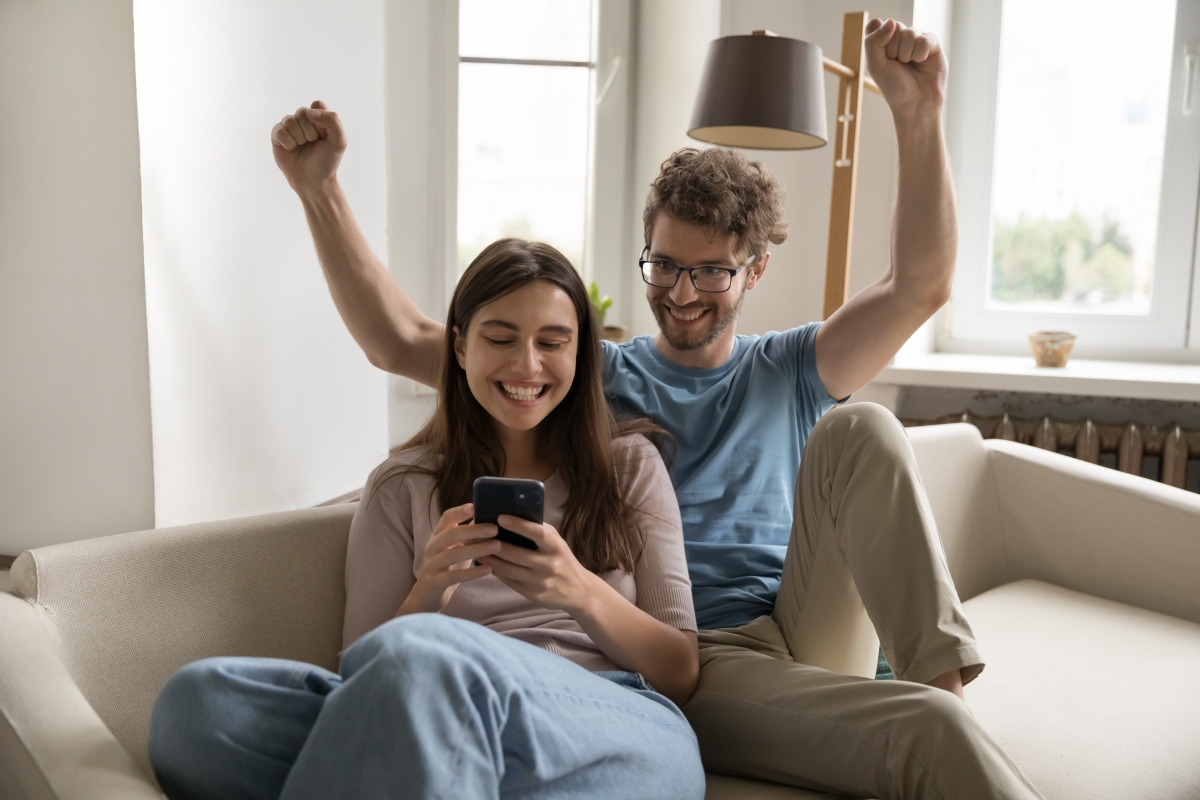 un jeune couple de primo accédants rennais heureux sur un canapé devant un smartphone