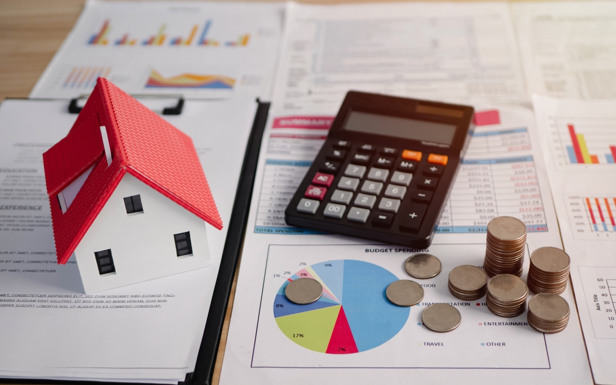 tva et lmnp – maquette de maison calculatrice et tas de pièces au dessus de documents de calcul
