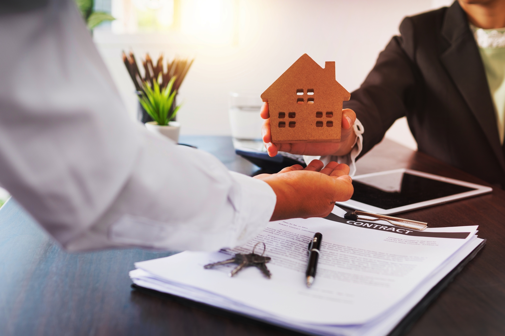 une main tendant une maison en bois à une autre devant un bureau