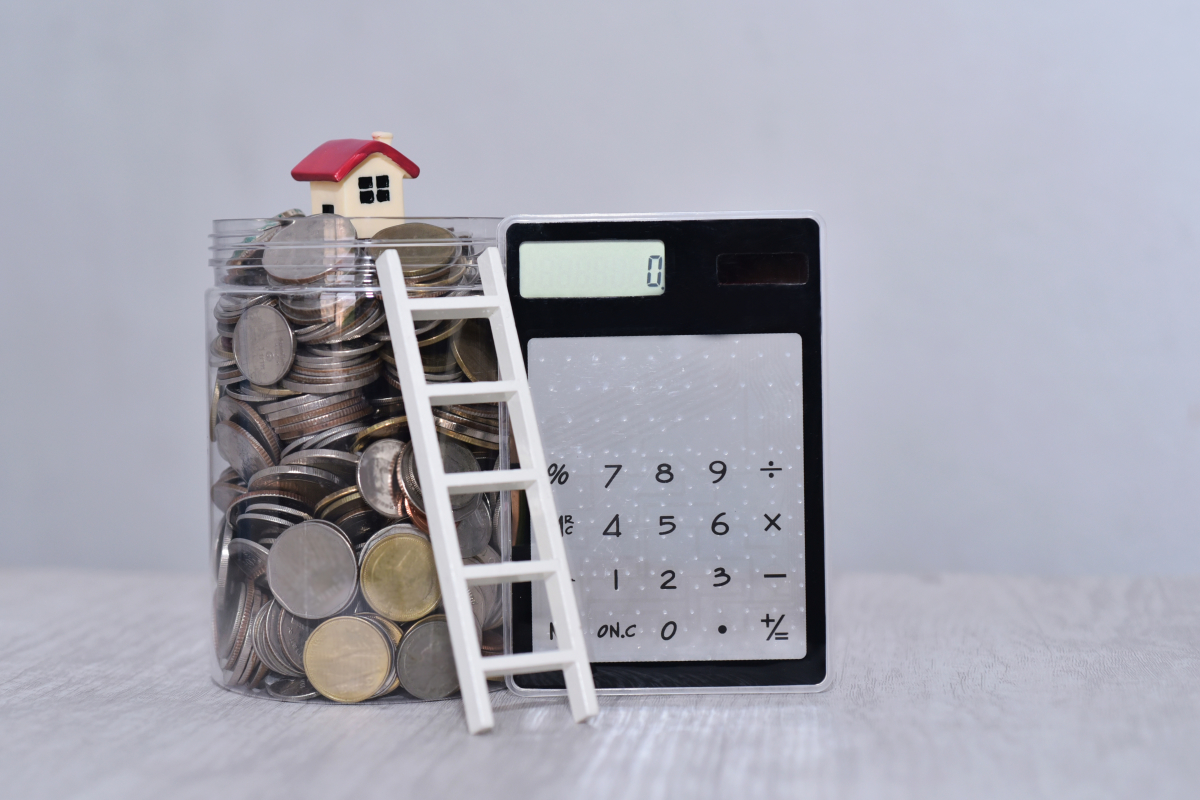 une calculette un pot en verre rempli de pièce surmonté d’une petite maison et d’une échelle