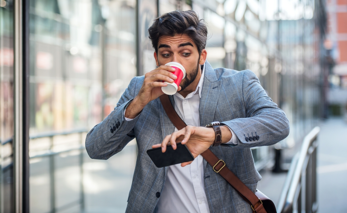 un homme en retard boit son café à emporter en regardant sa montre