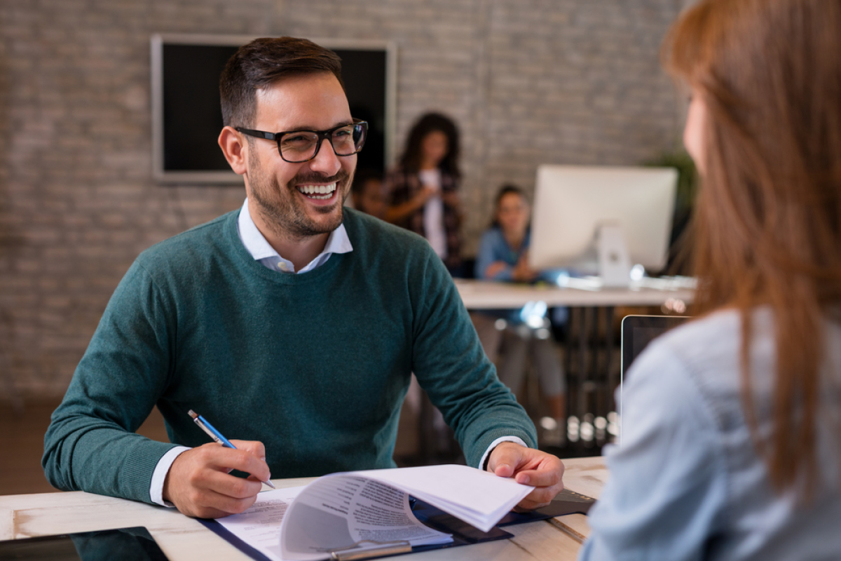 un homme souriant parle avec une femme de dos à un bureau