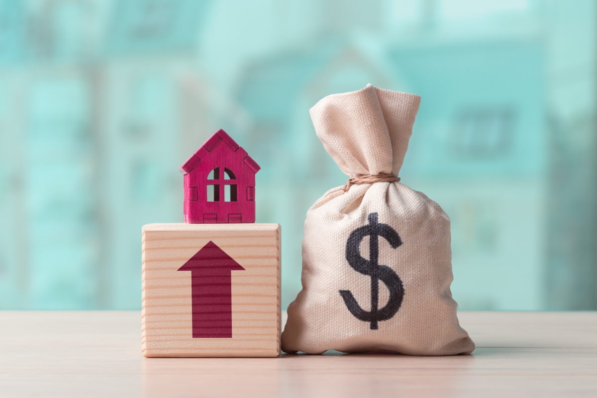 intérêts d'emprunt déductibles 2025 – un sac de jute marqué du signe $ un cube de bois avec une flèche rouge qui pointe vers le haut surmonté d'une maquette de maison rouge